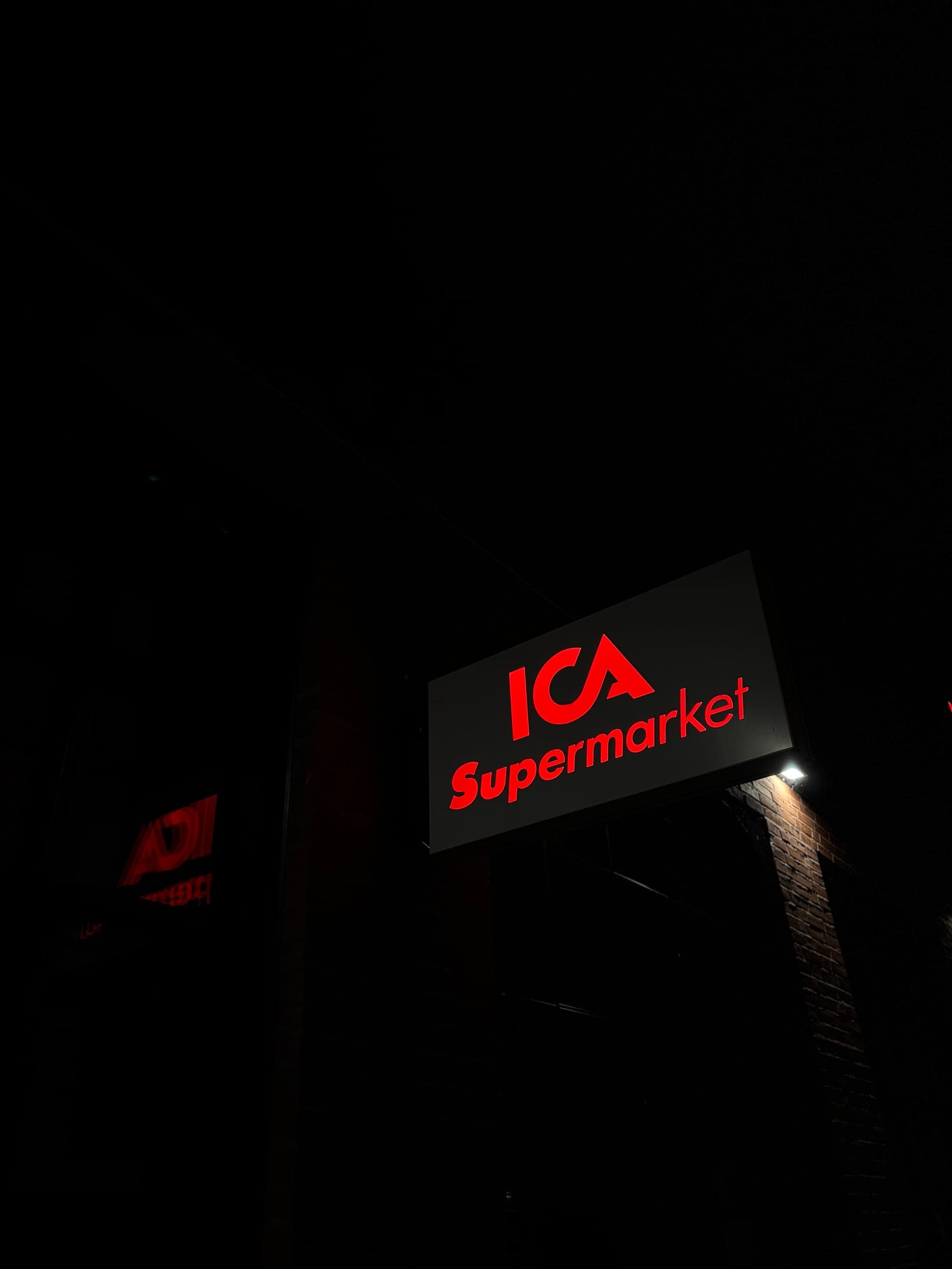 Flaggskylt som ljuslåda för ICA Supermarket i Stockholm, monterad vinkelrätt från tegelfasaden